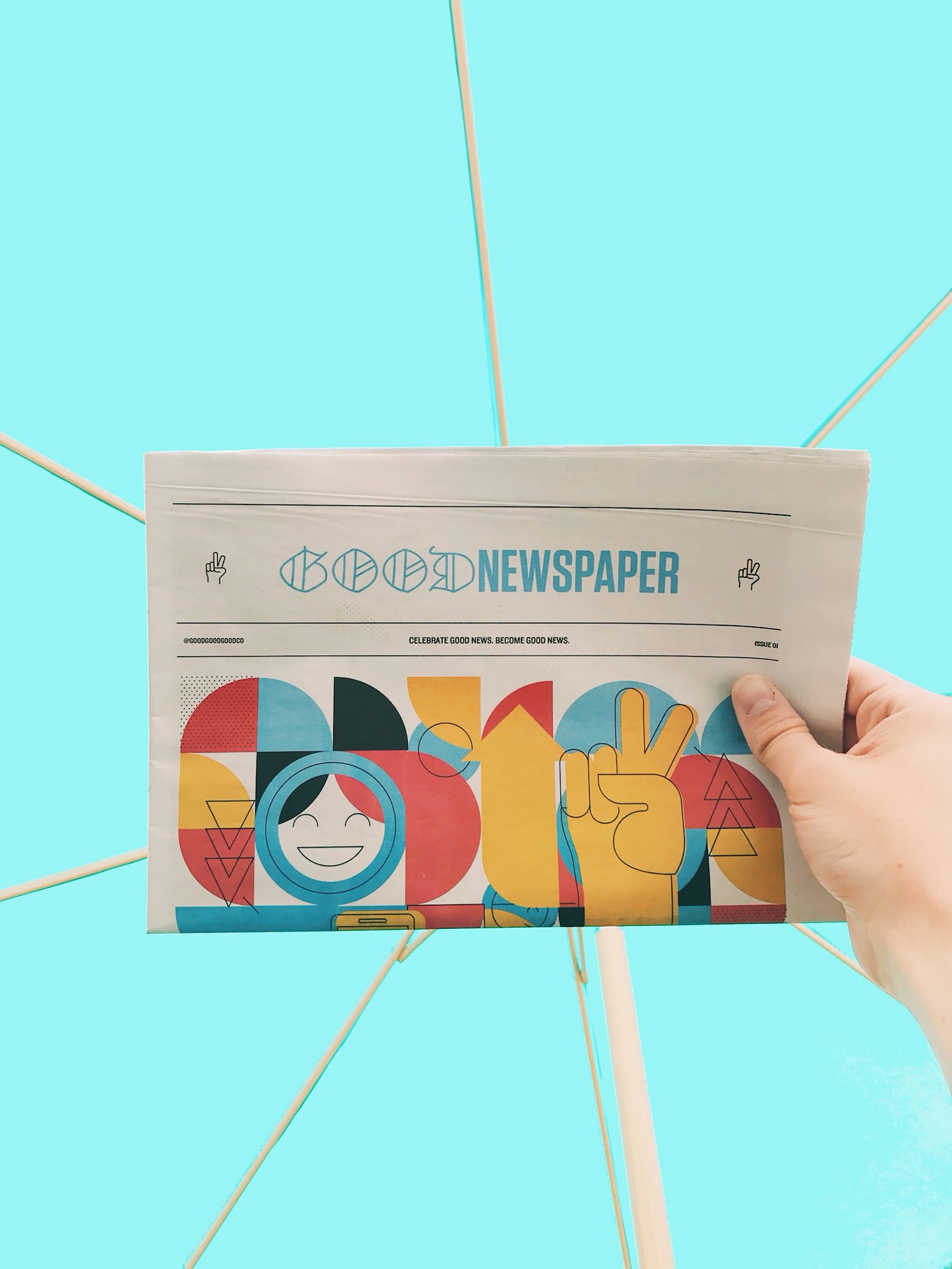 A hand is holding a newspaper with the headline 'Good Newspaper' in a modern design. The newspaper features colorful, abstract artwork with geometric shapes and a smiling face. The background is a sol