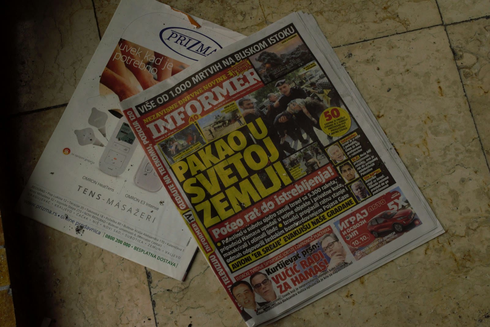 A newspaper is placed on a tiled floor. The headline in large yellow letters stands out. Next to it, there is an advertisement showing electronic massage devices. The overall setting seems casual and