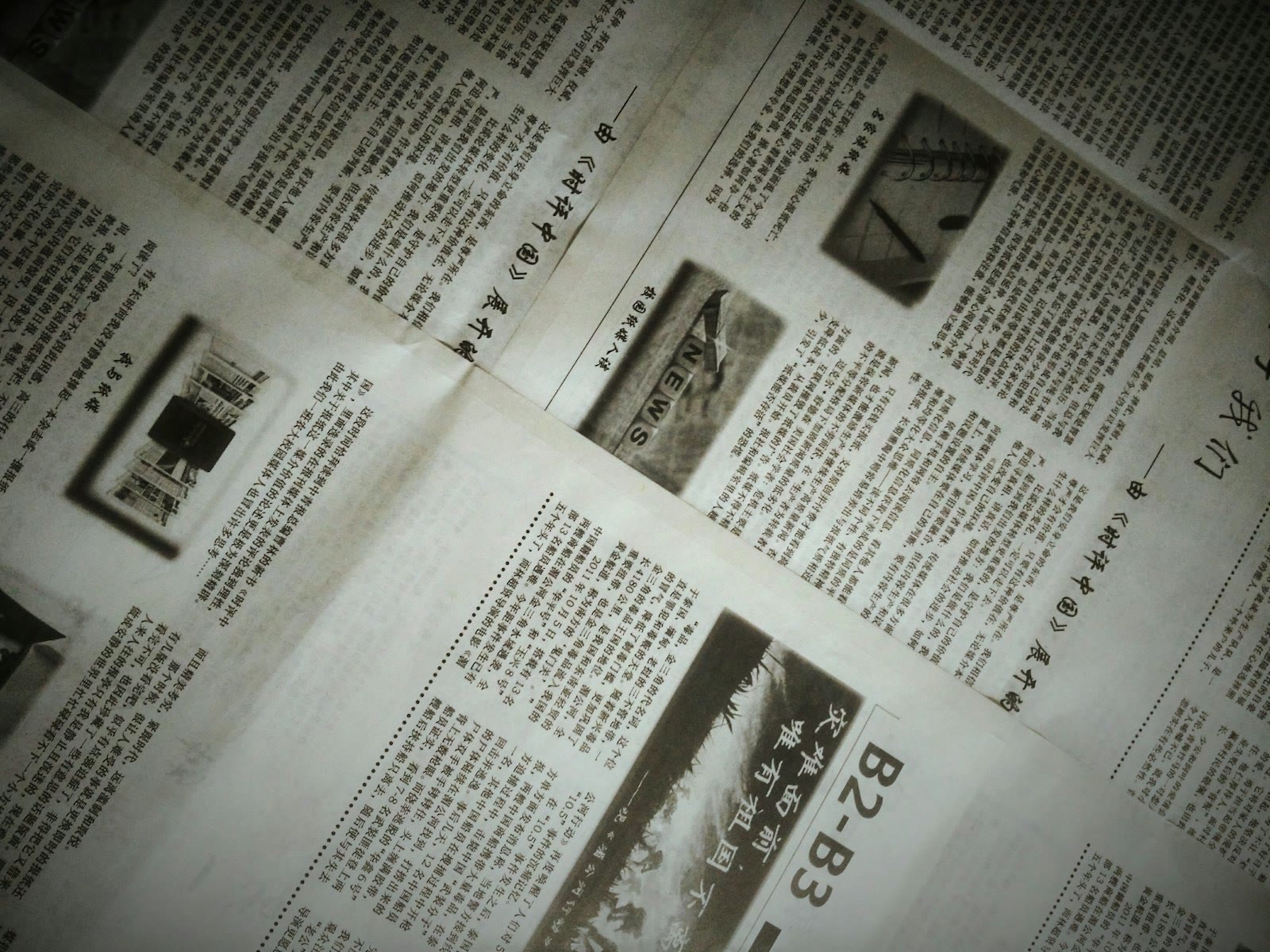 A close-up of a newspaper with multiple pages spread out. The text is written in a non-Latin script, possibly Chinese. There are also images within the articles, including one with the word 'NEWS'. Th